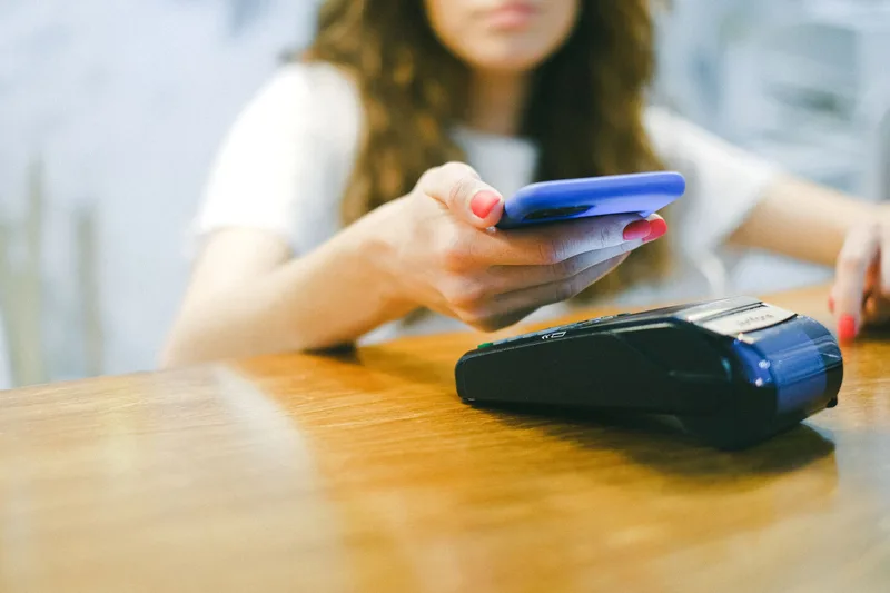 Person paying with a smartphone at a card payment terminal on a wooden table
