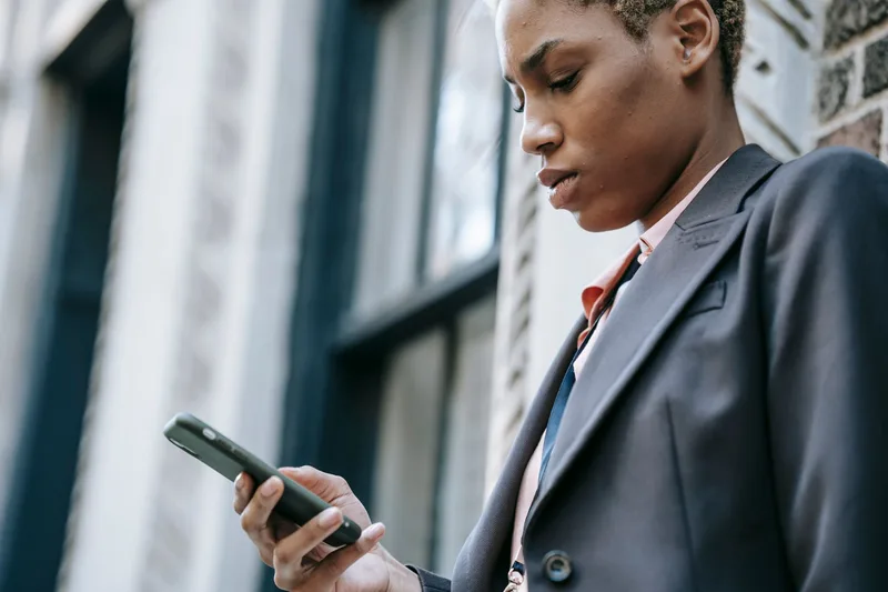 Person in a blazer looking down at a smartphone outdoors