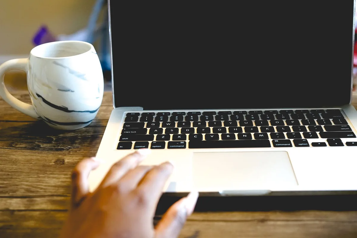 Hand typing on a laptop beside a coffee mug on a wooden desk