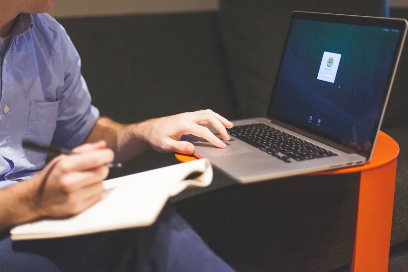 Person writing newsletter content on a laptop with a notebook open beside it