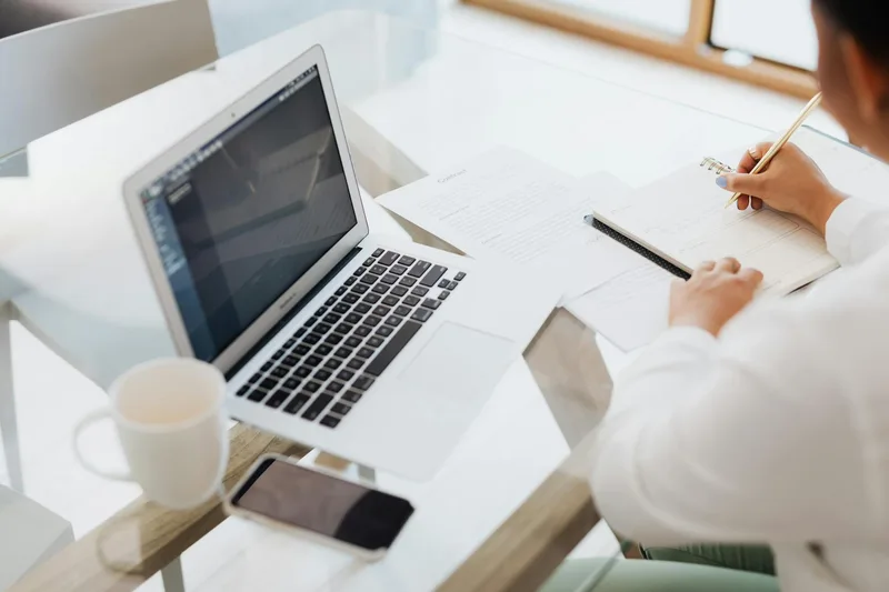 A solo creator writing email copy at a desk with a notebook open alongside a laptop