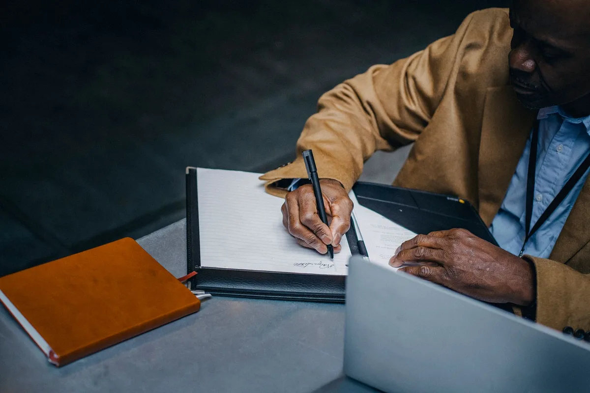 Person writing notes on paper near a laptop and diary while working at a desk, planning a funnel structure