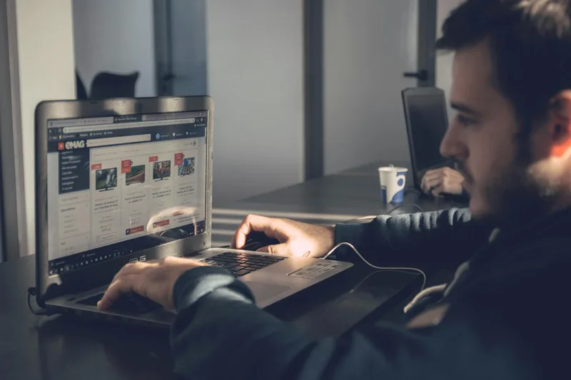 A person sitting at a desk, laptop screen showing a minimal webpage layout with one clear focal point, good natural light, focus on the screen