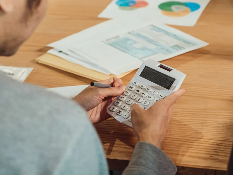 Person using a calculator with financial documents on a desk, representing the real cost math behind a percentage-based pricing model
