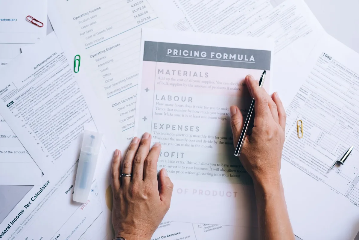 Hands organizing pricing documents and formula papers on a desk, representing the process of breaking down a tool&rsquo;s true cost