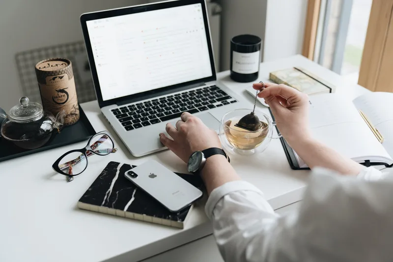 Laptop open to an email inbox on a desk with tea and a notebook nearby