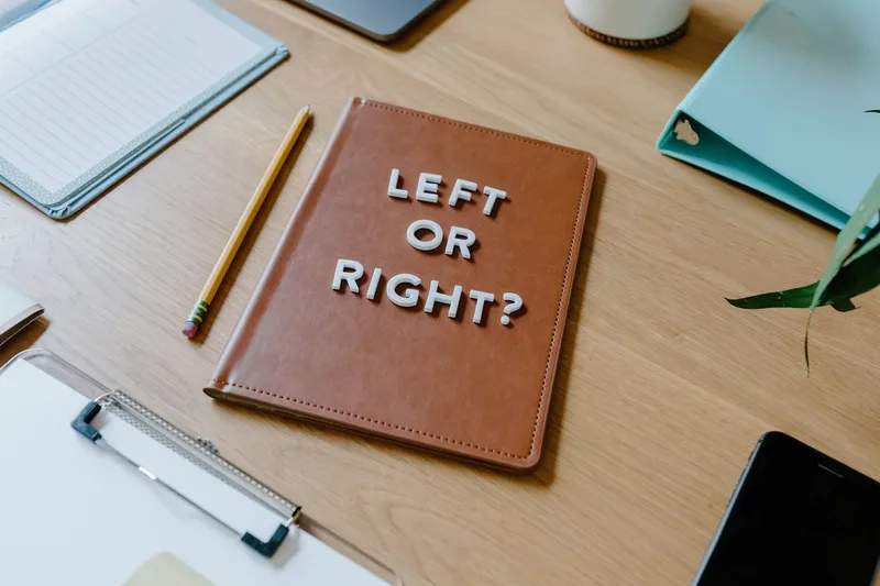 Notebook on a desk reading &ldquo;Left or Right?&rdquo; next to a pencil and clipboard