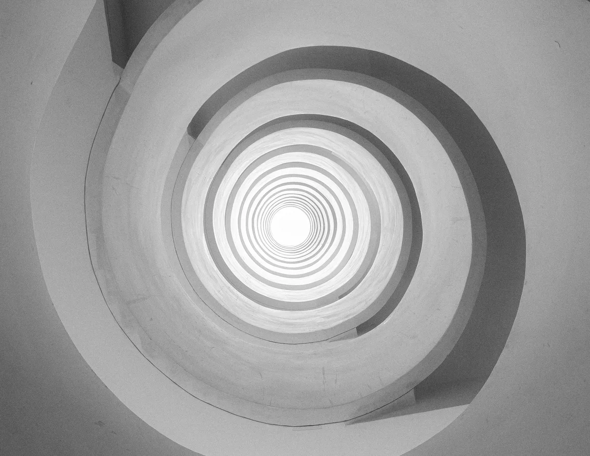 An abstract black-and-white photograph of concentric spiral rings narrowing to a single bright point, evoking the narrowing shape of a sales funnel
