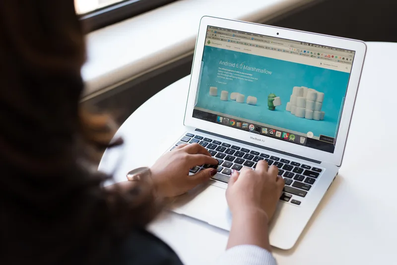 A person typing on a laptop at a white round table, representing the process of reviewing and rewriting landing page copy
