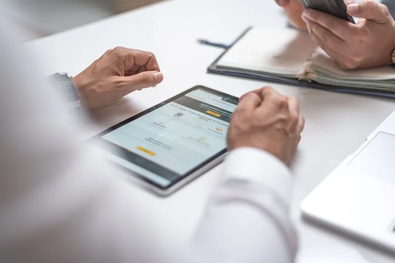 Two professionals review notes together using a tablet and smartphone