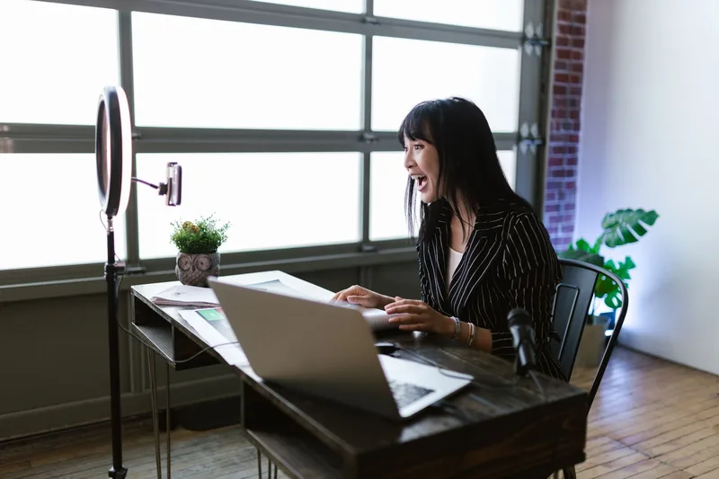 A course creator records a video lesson at a home desk setup with a ring light and laptop