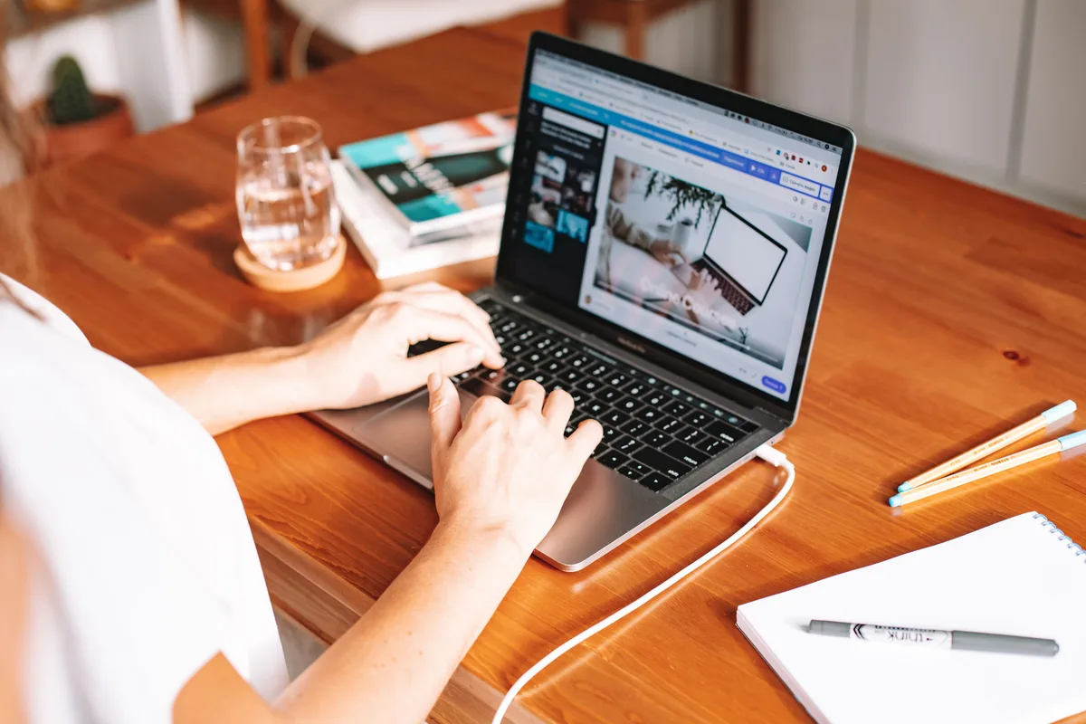 A creator types on a laptop at a wooden desk, researching course platform options