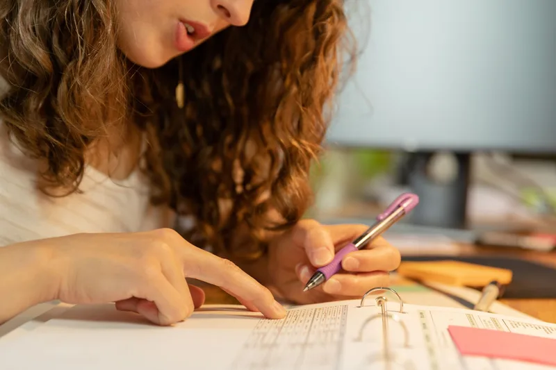 Person pointing at rows of numbers in a printed table while tracking data with a pen