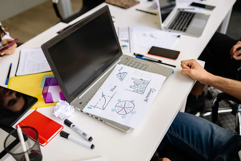Solo creator reviewing a funnel flow diagram on a whiteboard with laptop analytics open on the desk